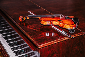 Violin with bow lying on piano on brown background