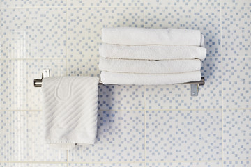 A stack of white clean towels in a hotel room. White towels lie on a shelf in the hotel's washroom.