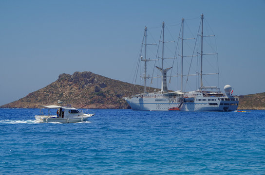 Luxus Segel Kreuzfahrtschiff vor griechischer Insel mit vier Masten und Wassersport Marina und Tenderboot und kleiner wei&szlig;er Yacht im Vordergrund