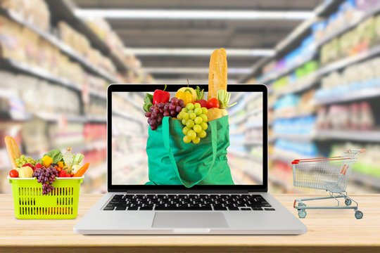 supermarket aisle blurred background with laptop computer and shopping cart on wood table grocery online concept