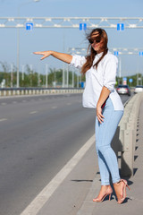 Fototapeta premium Pretty young woman hitchhiking along a road.