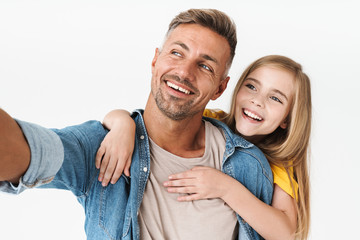 Fototapeta premium Image of beautiful caucasian father piggybacking her little daughter while taking selfie photo together