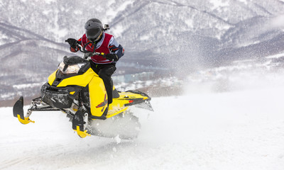 Fototapeta na wymiar man is flying on a snowmobile on a background mountains