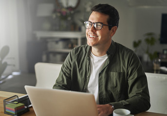 Smiling man with laptop sitting at desk looking away