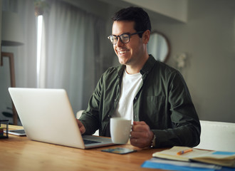 Fototapeta premium Man holding cup of coffee working on laptop