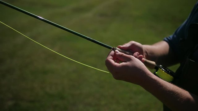 man fisherman, fishing, holding a fishing rod, stringing bait, spinning reel, on the street, by the river, standing on the shore on the green grass, Sunny weather, blue sky, summer, close-up