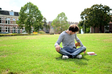 Naklejka na ściany i meble Smiling and happy Dutch student sitting with his cat in a park in a city in the Netherlands