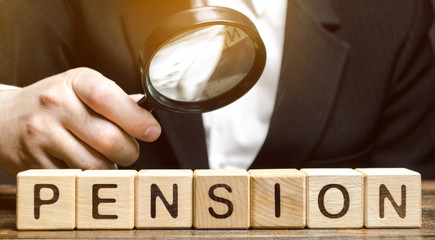 Wooden blocks with the word Pension and a magnifying glass in the hand of a man. Analysis of...