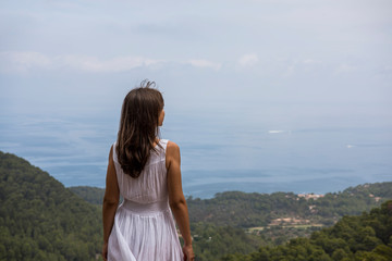 Fototapeta na wymiar Cap de Formentor, Mallorca, Spain. Young woman in front of beautiful scenery with the sea, rocks and cloudy sky.