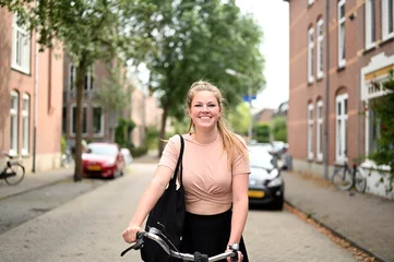 Fotobehang Smiling and happy Dutch woman riding a bicycle in a traditional street in Amsterdam, the Netherlands © Daniel Pieterson