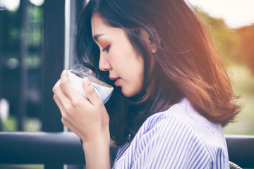 Close-up of a pretty girl with long hair Asians are drinking and inhaling the aroma of hot coffee, tea, green tea, espresso, latte. Mocha from a white ceramic coffee cup in the afternoon sunshine.