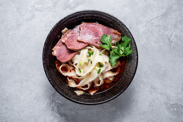 A bowl of nutritious and delicious beef noodles with noodles on a cement texture background