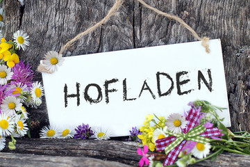 Schriftzug: Hofladen, auf Schild vor Holzhintergrund.