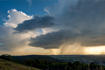 Fototapeta na wymiar Dunkle Gewitterwolken und aufstseigende weiße Wolken mit letztem blauen Himmel und Regen bei Sonnenschein am Horizont über Weißenburg in Bayern