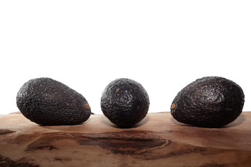 three avocados on a wood with white background