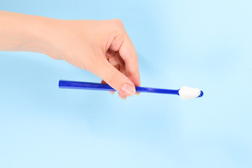 Woman holds toothbrush with toothpaste in her hand on a blue background.