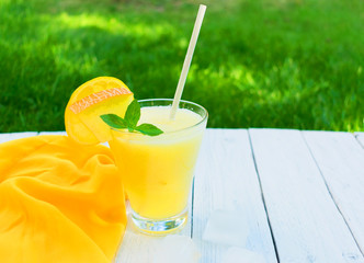  Bright melon smoothie with mint and lemon on a background of fresh green grass. Copy space. Concept of summer cooling drinks.