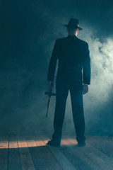 Retro gangster stands with machine gun in smoky room. Rear view. - obrazy, fototapety, plakaty