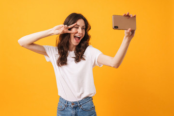 Positive optimistic smiling young woman posing isolated over yellow wall background take a selfie...