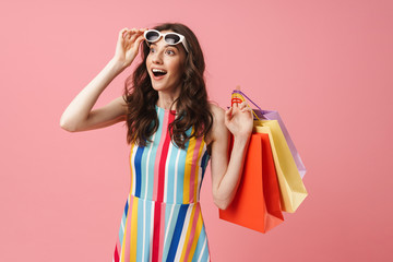Beautiful pleased positive happy young cute woman posing isolated over pink wall background holding shopping bags.