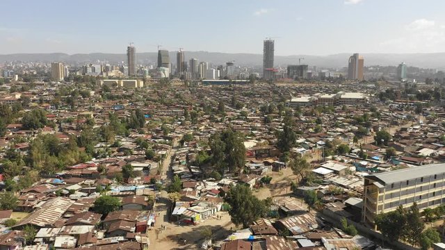 Flying over poor residential neighborhoods with rooftops made of corrugated sheet, contrast with looming modern skyline of Addis Ababa, urban development in Ethiopia Africa