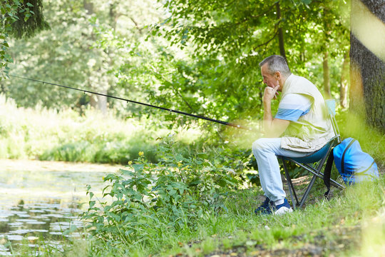 Mature man sitting on chair near the river outdoors and fishing alone