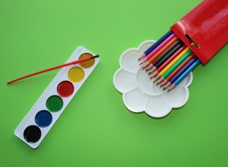 paint, eraser, pencils on a green background. Watercolor and colored objects for school and...