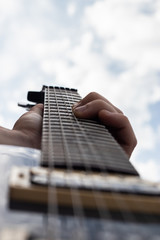 Male hand playing electric guitar and bending the strings with blue cloudy sky in the background