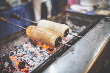 Chimney cake rolls spinning over hot coals at market stand.