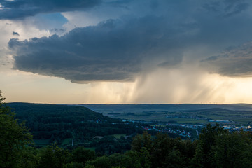 Dunkle Gewitterwolken mit letztem blauen Himmel und Regen bei Sonnenschein am Horizont über Weißenburg in Bayern