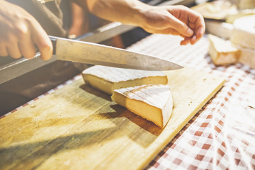 Man cutting cheese with knife on wooden board at street market food festival.