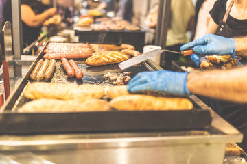 Man hands grilling sausages and warming buns on professional bbq on the street. Fast food concept.