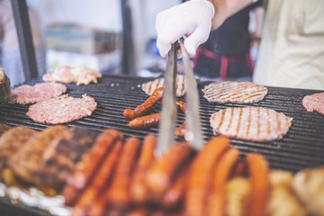 Man preparing burgers and sausages at street festival.
