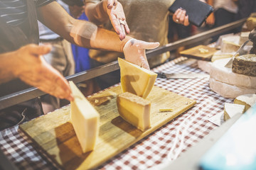 Man preparing cheese slices on wooden board at street market.