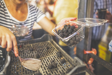Seller selling blackberries by making portion in plastic container.