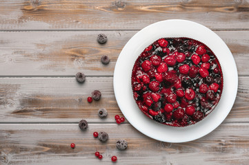 Pie with berries top view: raspberry, currant, strawberry on a white plate on a wooden background, near red currant and cherry berries
