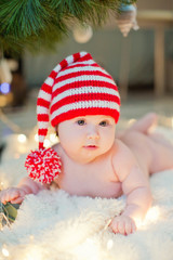 newborn baby in red knit hat near Christmas tree with lights