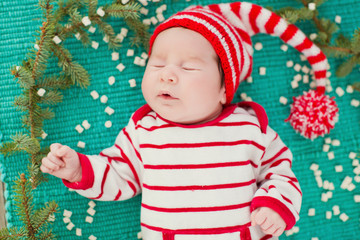 newborn baby in red striped costume near Christmas tree