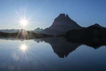 The sun and the Midi d'Ossau peak are reflected in Lake Gentau at dawn, Pyrenees of France