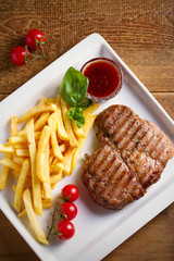 Grilled pork steak with fries, sauce and vegetables on white plate