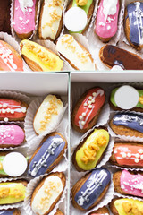 many tasty multi-colored eclairs lie in a box on a wooden table