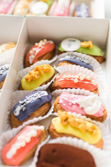 many tasty multi-colored eclairs lie in a box on a wooden table