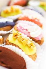 many tasty multi-colored eclairs lie in a box on a wooden table