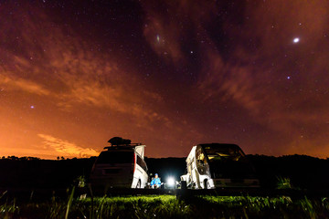 Campervans are parked on a beach at night under stars.