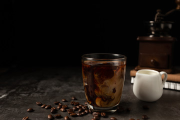 Milk pouring into iced black coffee on table and black background.