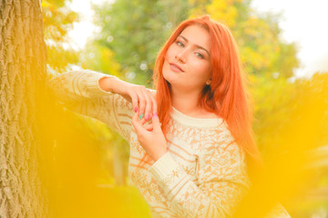 close-up portrait outdoor with beautiful young woman in warm fall sweater near yellow autumn leaves
