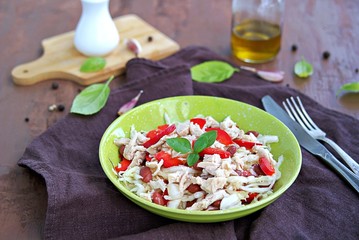 Salad of white cabbage, boiled chicken, red sweet pepper and brown beans in a green bowl on a brown concrete background. Healthy food.
