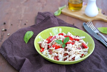 Salad of white cabbage, boiled chicken, red sweet pepper and brown beans in a green bowl on a brown concrete background. Healthy food.