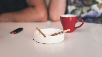 Two medical marijuana joins are in the ashtray, a cup of coffee and lighter near. Smoking marijuana joint indoors.