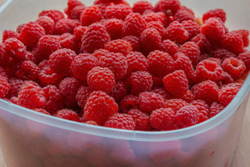 ripe red raspberries  in a plastic container on a wooden background as a natural background